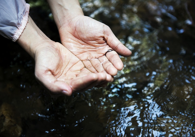 Two hands grabbing water from a small and clean lake