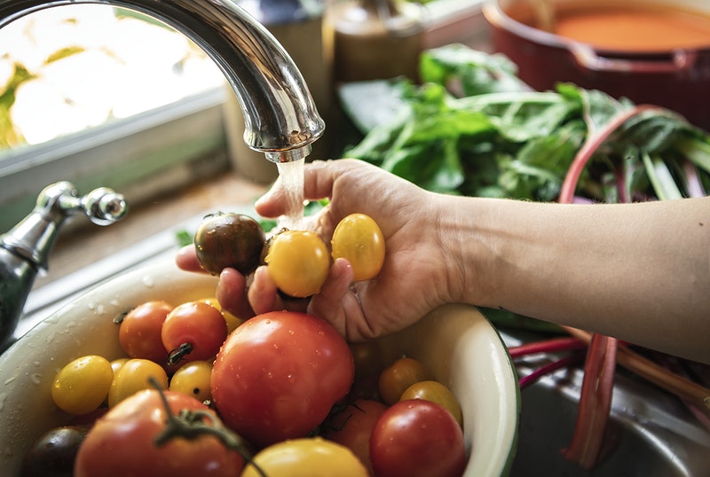 A person's hand washing vegetables in the kitchen's sink