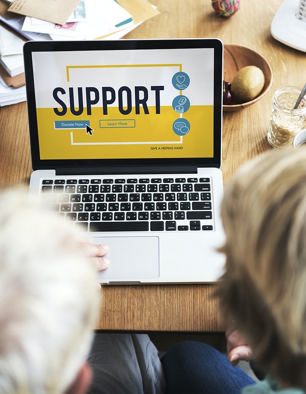 Two people working with an Apple MacBook with the word "Support" displayed on the screen