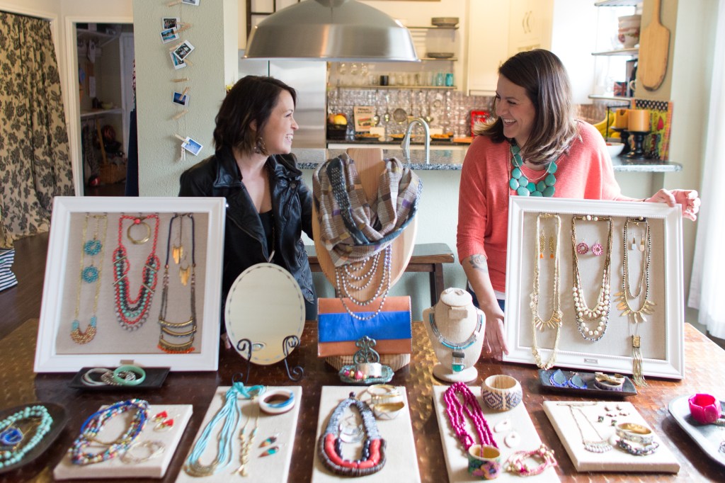 Two women artisans looking at each other smiling while displaying their beautifully-designed products