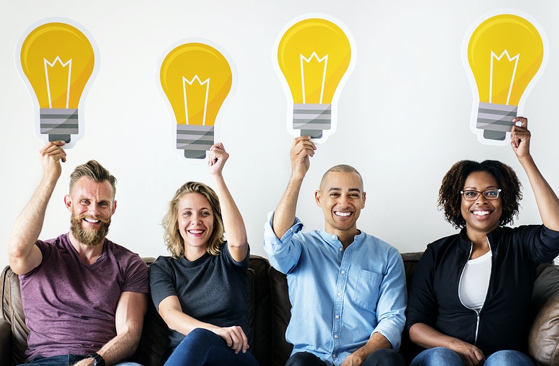 Two women and two men each holding a big image of a lightbulb while smiling to demonstrate how diversity leads to greater creativity