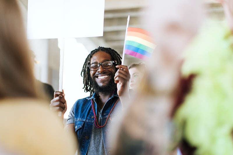 An African American smiling and holding a flag of different colors to represent diversity and inclusion