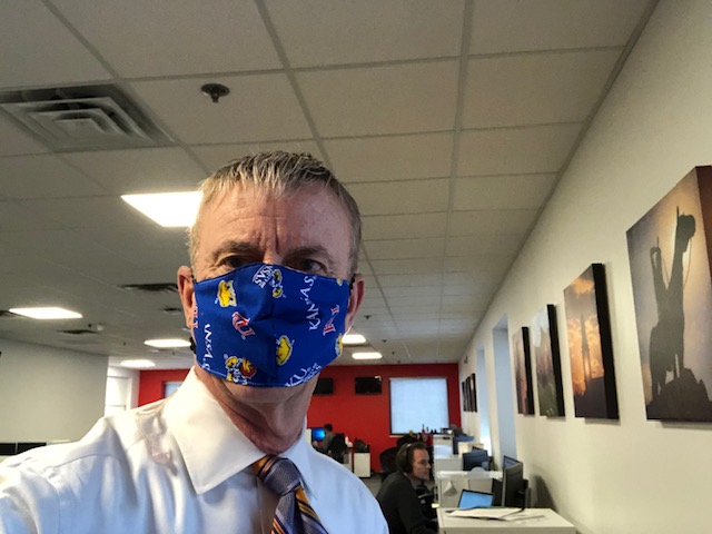 Journalist John Holt using a mask from the University of Kansas while at his work as an anchor and reporter